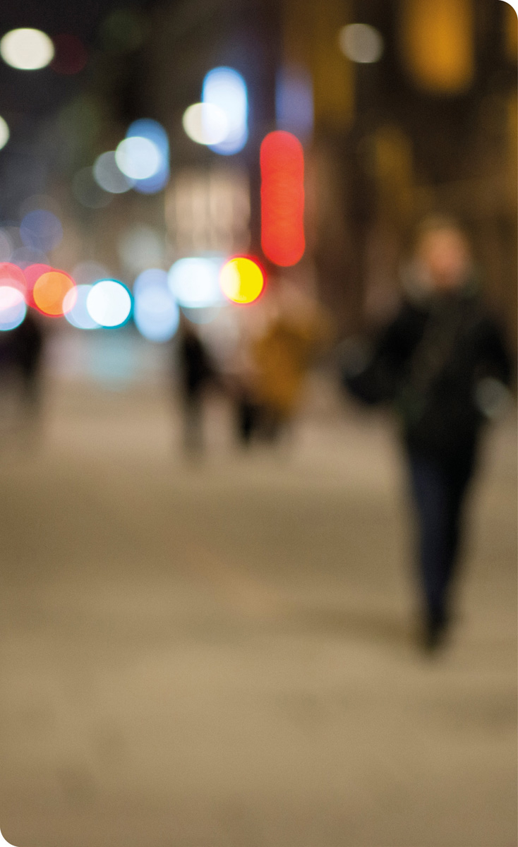 Bilde av en uskarp bygate kveldstid med mennesker, lys fra gatelys og andre lys fra trafikken.