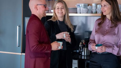 Tre blide ansatte ved kaffemaskin
