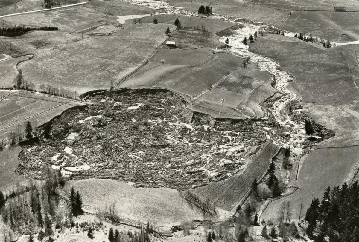 Skredet ved Borgen i Ullensaker i desember 1953. Den tilnærmede sirkelformede skredgropa hadde smal skredport som den omrørte kvikkleira rant ut gjennom. Leira fulgte bekkeløpet og demmet opp flere bekker. Foto: Fjellanger Widerøe.