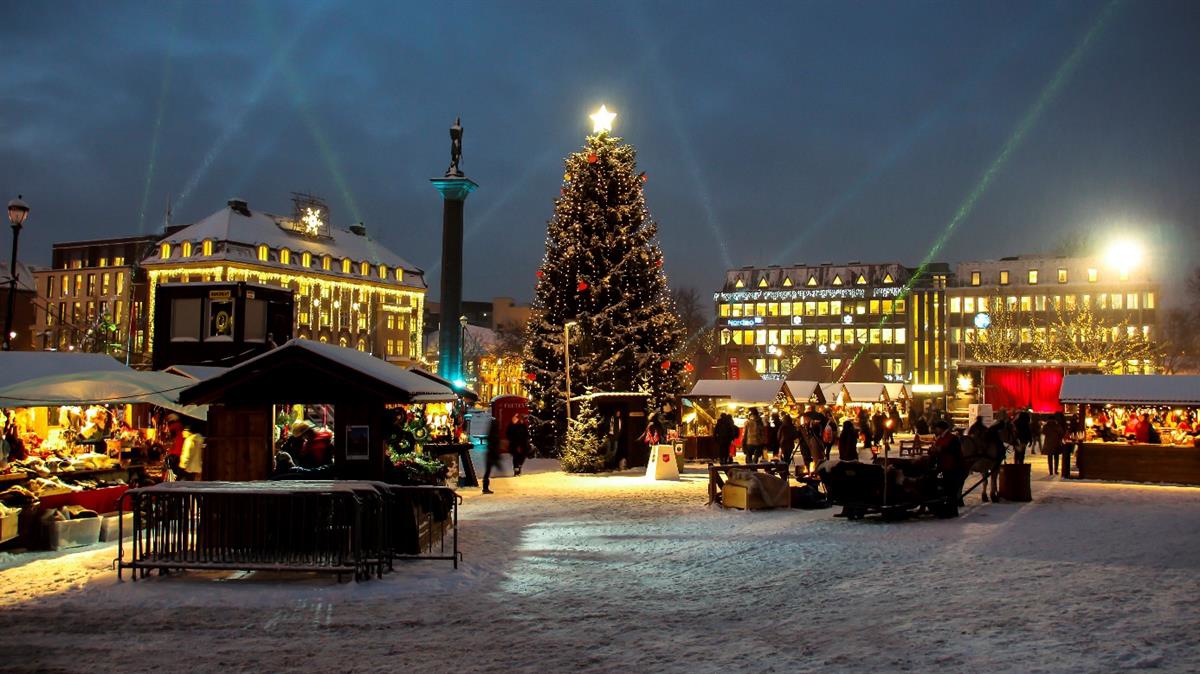 Juletorg med marked og folkeliv om kvelden, juletreet er tent og det er litt snø.