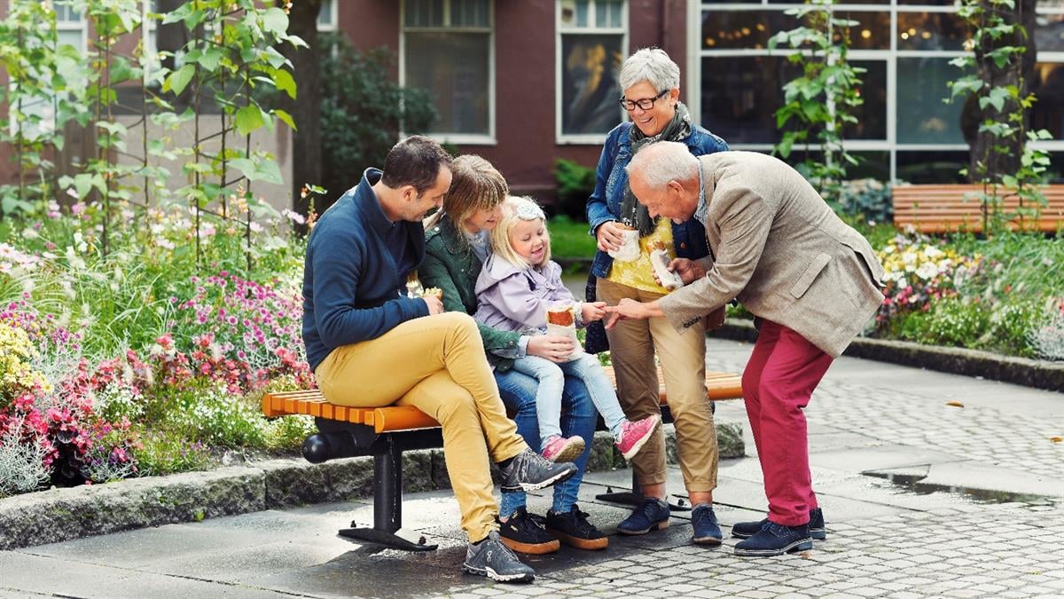 Flere generasjoner sitter på benk i sentrum.