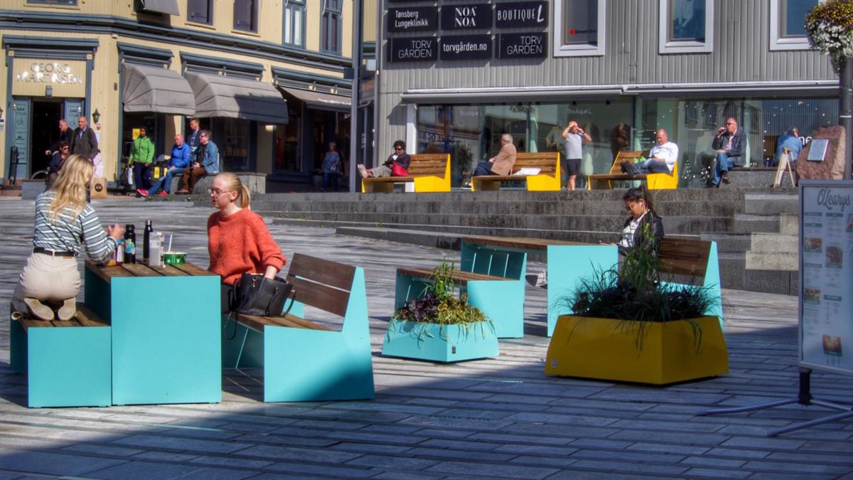 Bymøbler av tre og blåmalt metall i sentrum.