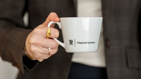En dame som holder en hvit kopp med Departementene på