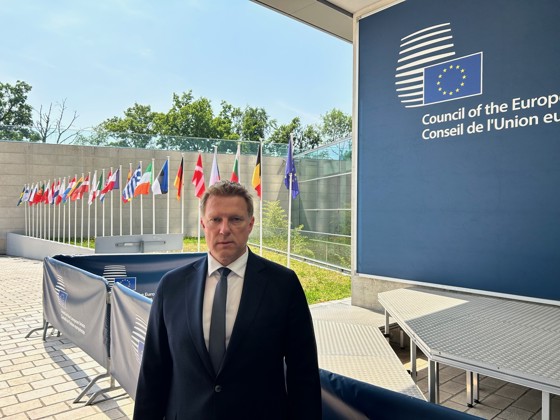 Joakim Øren foran mange flagg og en blå vegg der man ser EU-flagget.