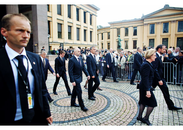 Figur 10.12 Medlemmer av kongefamilien, AUFs leder, og representanter fra det offisielle Norge omgitt av livvakter etter å ha signert kondolanseprotokollen i Universitetets aula 25. juli.
