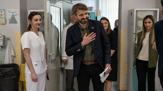 Jan Christian Vestre places a flat hand on his chest inside the heart hospital in Kyiv. A white-clad Ukrainian healthcare worker stands beside him, along with other medical staff.