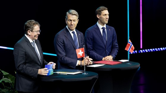 Switzerland's Minister of the Environment, Transport, Energy and Communications Albert Rösti, Minister of Energy Terje Aasland and Minister of Climate and Environment Andreas Bjelland Eriksen on the stage. There is a table in front of them, with the flags from Norway and Switzerland, in addition to the agreement signed.