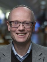 Mann med briller og grå jakke.