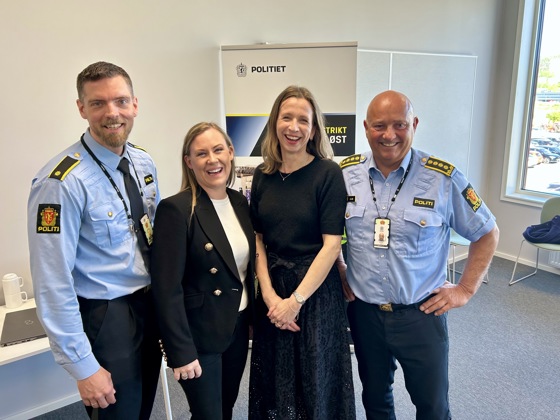 To kvinner kledt i svart flankert av to menn i blå uniformsskjorter.