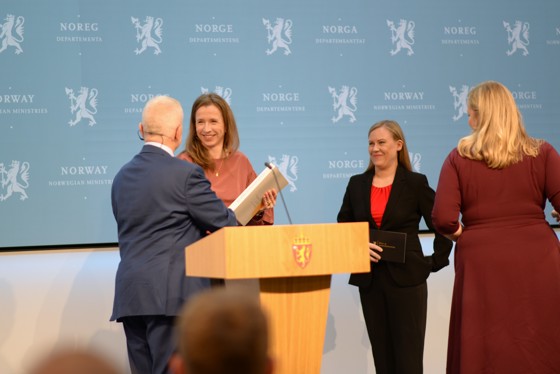Mann overleverer rapport til kvinne, med to andre kvinner til stede.