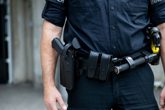 Nærbilde av midtpartiet til en person kledt i mørkeblå uniform. I beltet har har pistol og annet utstyr.