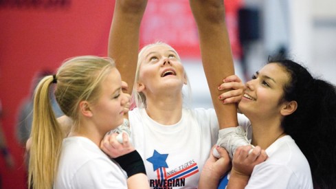 Tre cheerleading-jenter står i base og holder en fjerde jente som vi bare ser beina til.