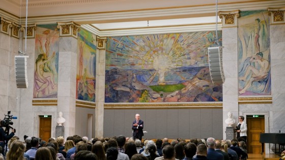 Statsminister Støre står i Aulaen foran en fullsatt sal med studenter.