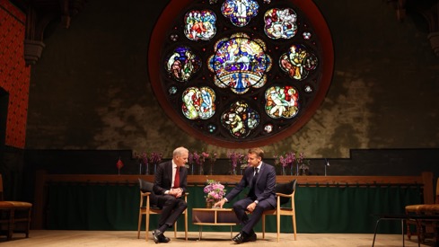 Emmanuel Macron og Jonas Gahr Støre sitter i hver sin stole i samtale foran et glassmaleri i Akershus Slott.