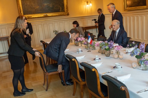 President Macron setter seg til bords i Parkveien 45, der statsminister Støre allerede sitter. Hvit duk og franske og norske bordflagg.