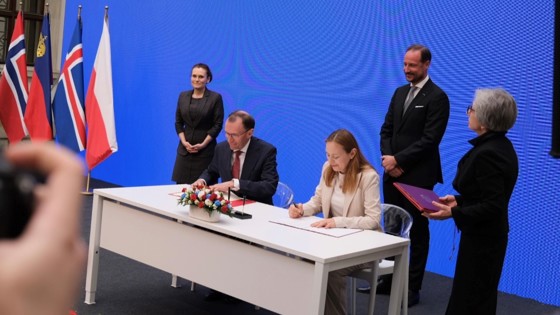 Bilde av utenriksminister Eide og Polens minister for regional utvikling og fond sittende for å signere, med kronprins Haakon stående bak.