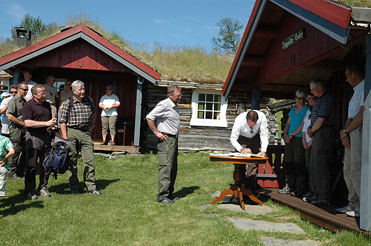 HKH Kronprins Haakon signerer seterboken på Nygjeltsetra hos Liv Erna og Helge Nygjelten, fulgt av Per Ousten. Foto: LMD
